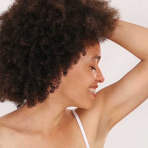 A side profile of a smiling woman raising her arm to reveal smooth, hair-free underarm skin. The image represents the results of professional laser hair removal treatments for long-lasting hair reduction and smoother skin.